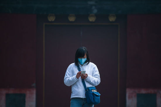 2014年10月24日,北京地坛公园一位戴着口罩的女士正在查看手机。当日,中央气象台继续发布霾黄色预警,京津冀地区仍有中度、重度霾。